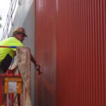 Worker Applying Lithium Concrete Coating On Red Industrial Wall